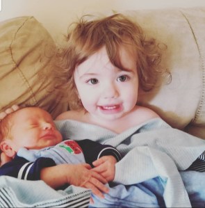 16 Month old curly hair girl holding her newborn brother