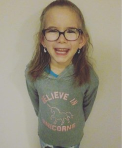 6 year old Hailey with her brown hair in a pony tail, wearing glasses, and smiling.