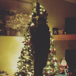 Lit up Christmas tree with a silhouette of a dad holding his infant baby boy in front.