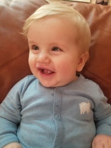 Timothy sitting on the couch smiling. He is wearing a blue sleeper with a polar bear on it. 