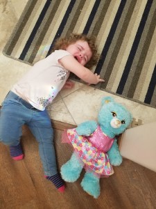 Charlotte laying on the ground throwing a tantrum beside a teddy bear.