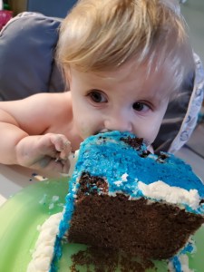 Timothy on his first birthday leaning mouth first into a corner of his blue birthday cake.