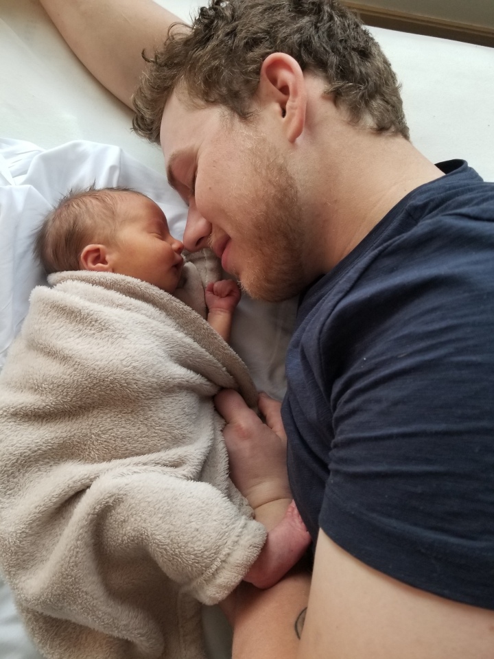 A photo from the hospital when Timothy was a newborn. James is laying beside him on he bed. they are facing each other with their eyes closed.