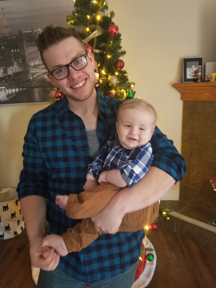A photo of James and Timothy in front of the Christmas tree wearing blue plaid shirts.