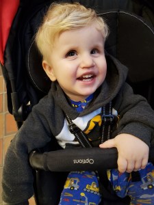 Photo of Timothy sitting in his stroller with a big smile on his face. 