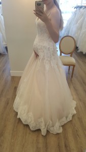 Melissa standing in a wedding dress cradling her baby bump.