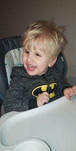 Photo of Timothy in a batman outfit in his highchair smiling